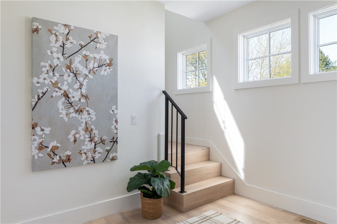 Staircase with floral artwork, windows, and potted plant, bathed in sunlight.