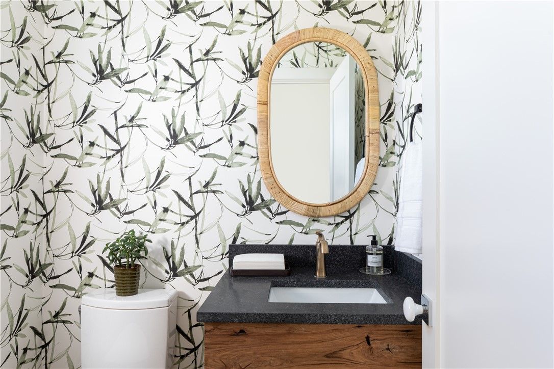 Small bathroom with bamboo print wallpaper, wooden vanity, oval mirror, and toilet.