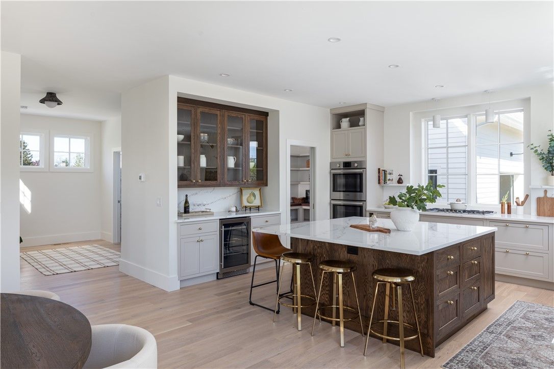 Spacious kitchen with large island, wood cabinetry, and stools. Built-in wine cooler and bar area, white walls.