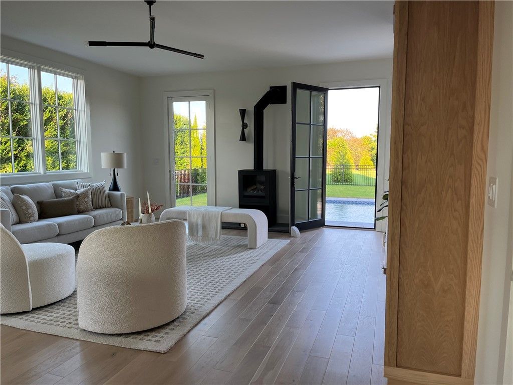 Living room with light wood floors, white walls, and French doors leading to a yard. Furnishings in neutral tones.