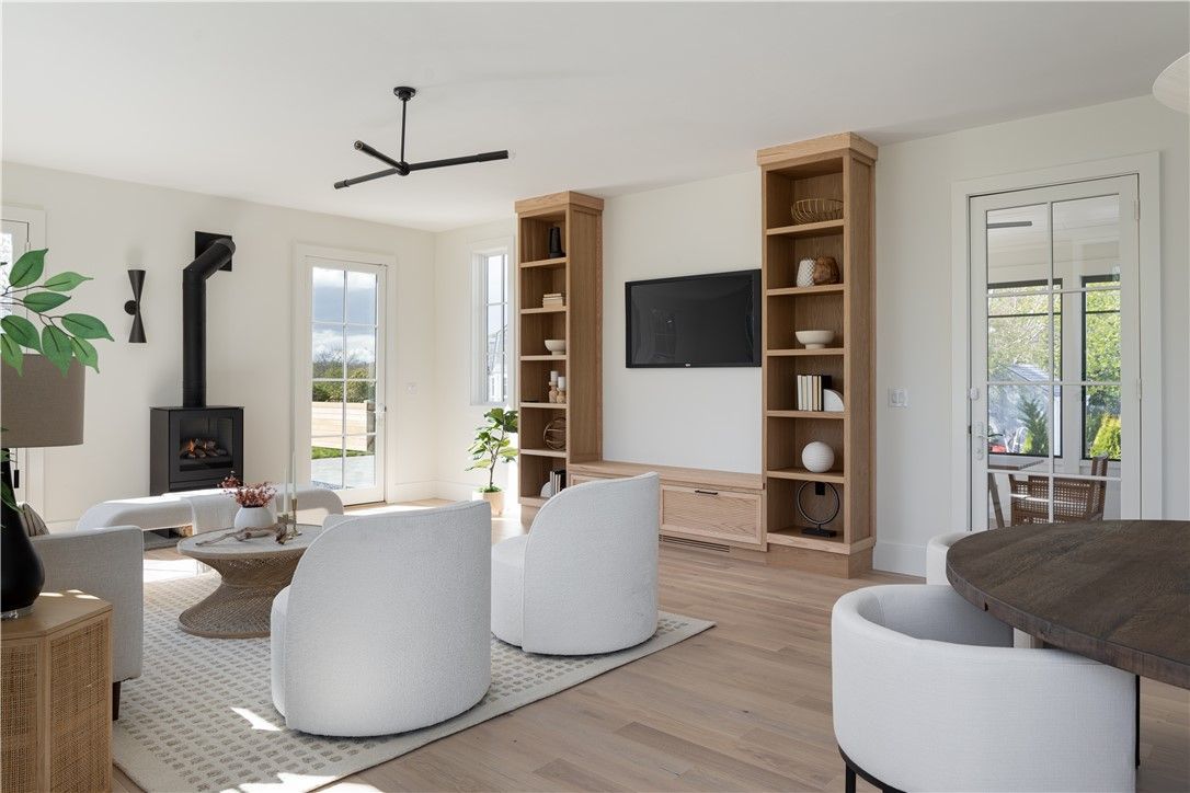 Bright living room with white walls, wood floors, a fireplace, bookshelves, and two white chairs.