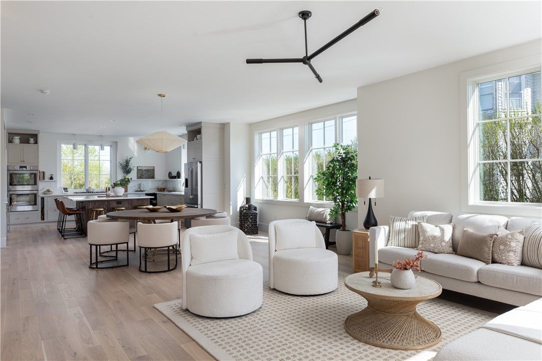 Bright, open-plan living space with white walls, light wood floors, and neutral-toned furniture. 