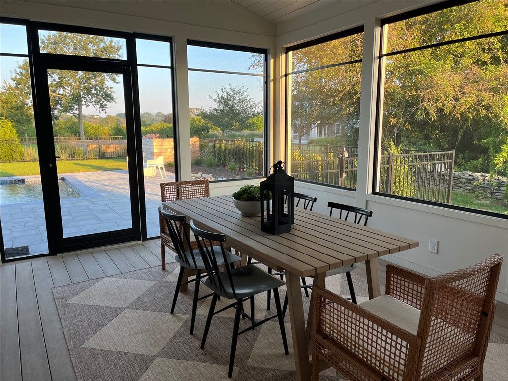 Screened porch with dining table, chairs, and garden views through windows.