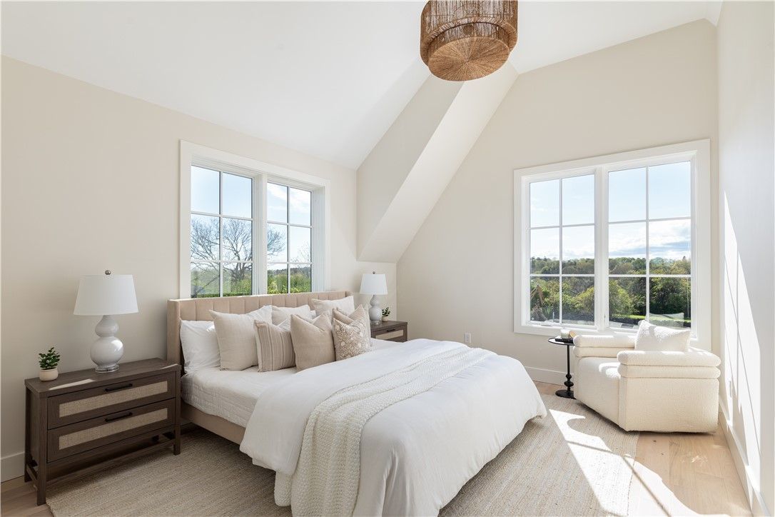 Bedroom with bed, windows, and armchair; neutral tones.