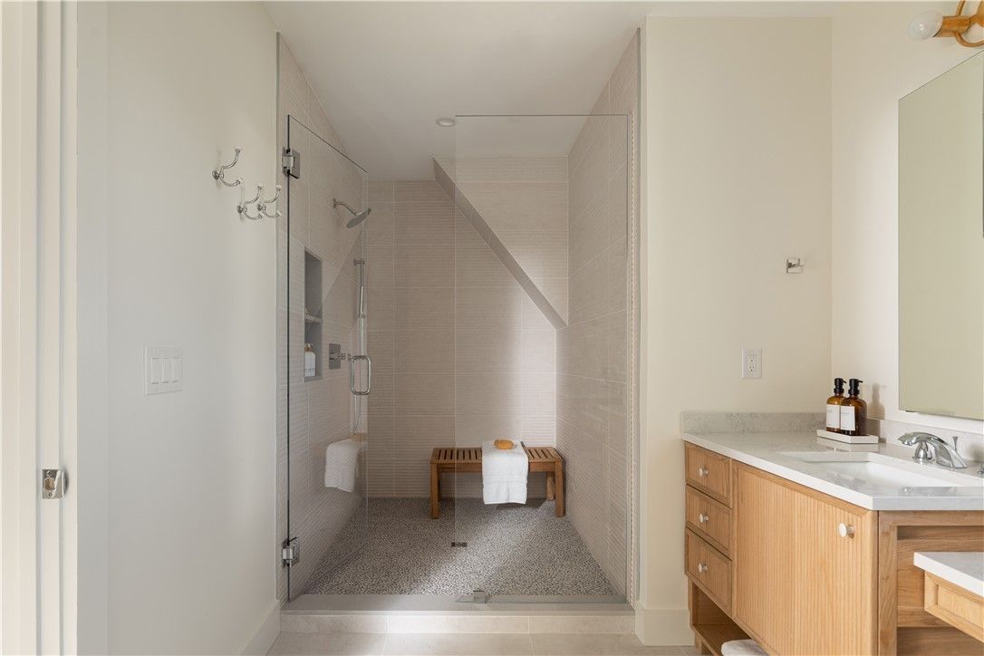 Bathroom with a walk-in shower. Light wood vanity, white walls, and pebble floor in the shower.