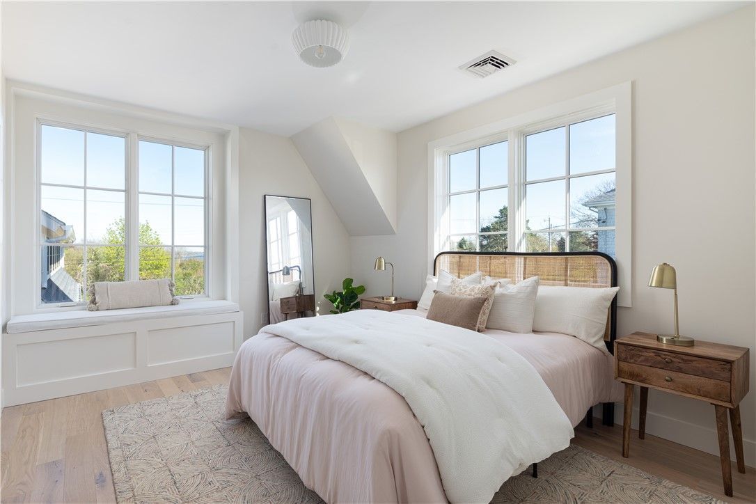 Bedroom with bed, windows, light wood floors, and neutral color scheme.