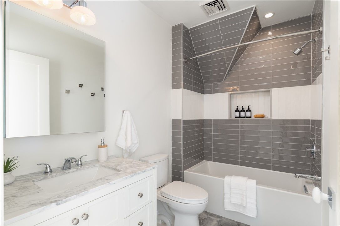 Modern bathroom with gray and white tile, a bathtub, toilet, and sink.