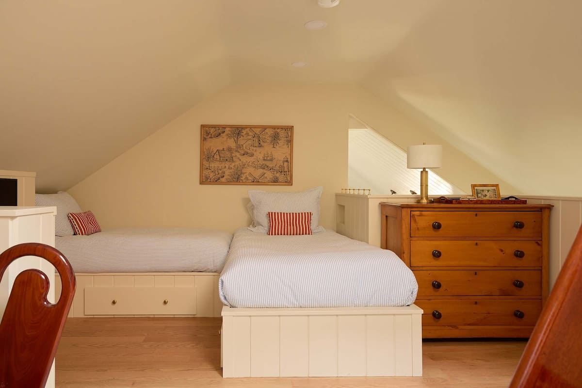 Cozy attic bedroom with two twin beds, wooden dresser, and a wall map. Soft lighting.