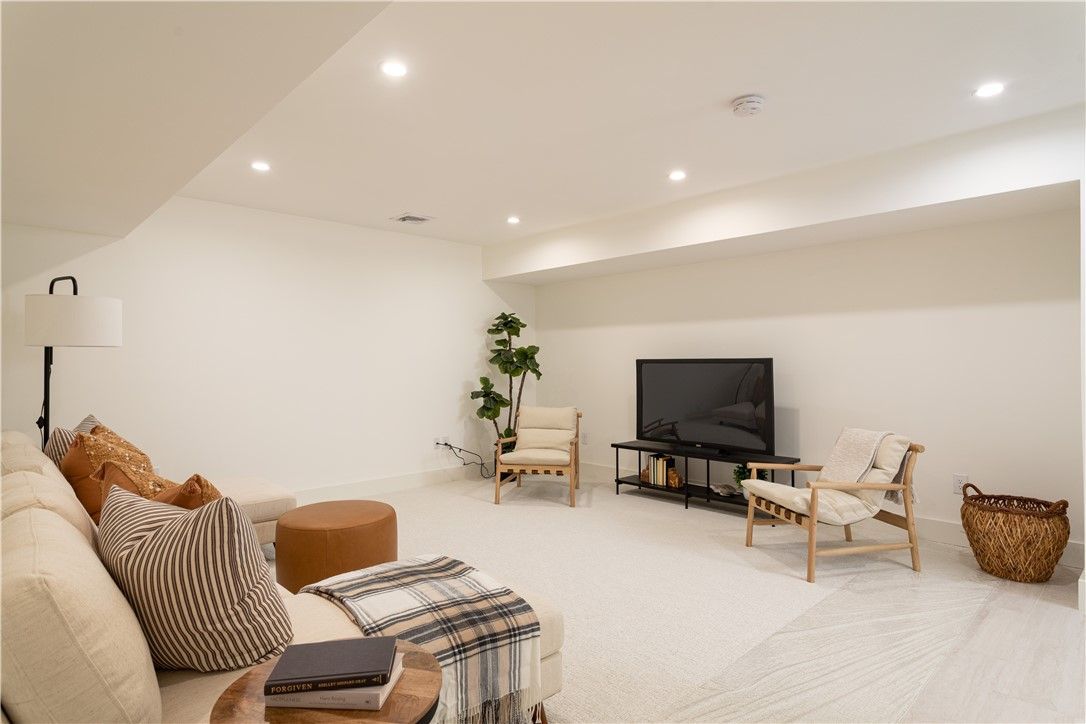 Cozy living room with off-white walls, carpet, and furniture. A sectional sofa, chairs, and a TV are present.