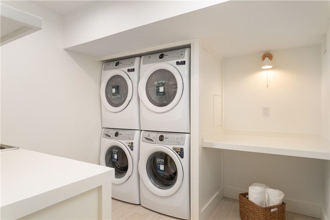 White laundry room with stacked washer and dryer, shelf, and a basket of towels.