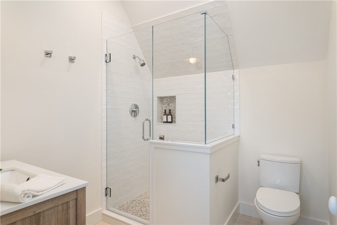 White bathroom with a glass shower enclosure, toilet, and vanity.