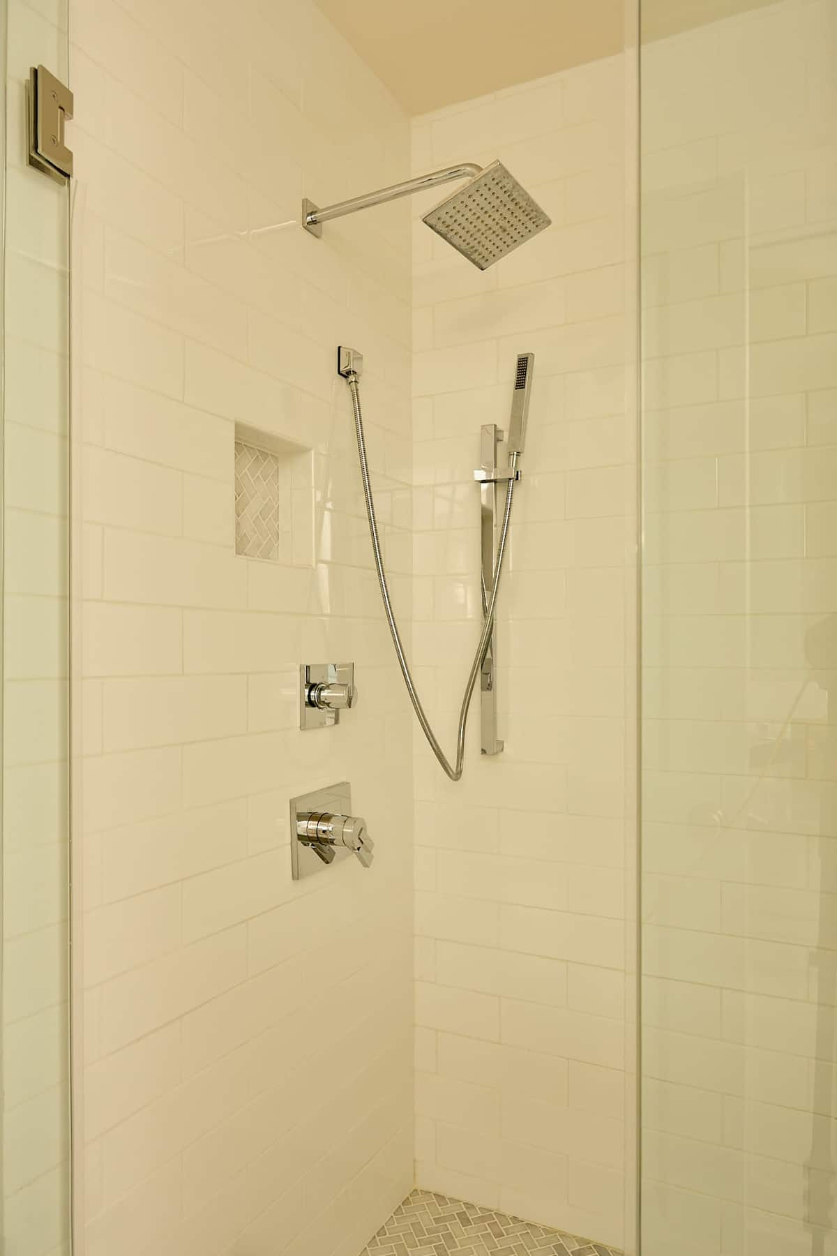 White tiled shower with glass door and silver fixtures.
