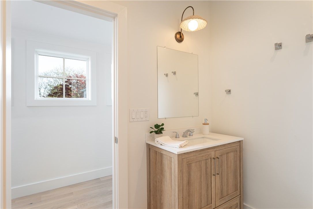 Bathroom with wood vanity, mirror, window, and wall-mounted light fixture.