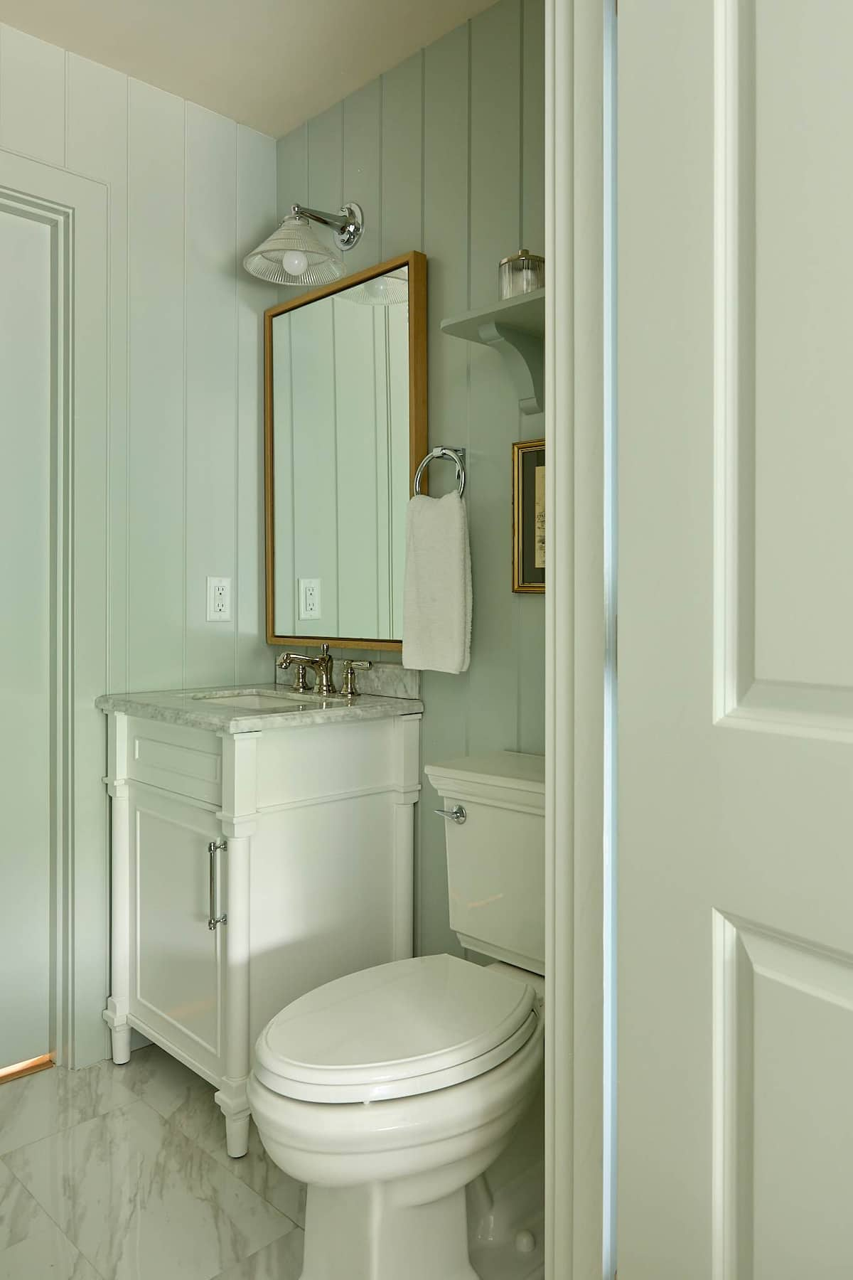 Small bathroom with a white vanity, toilet, and light green vertical paneling.