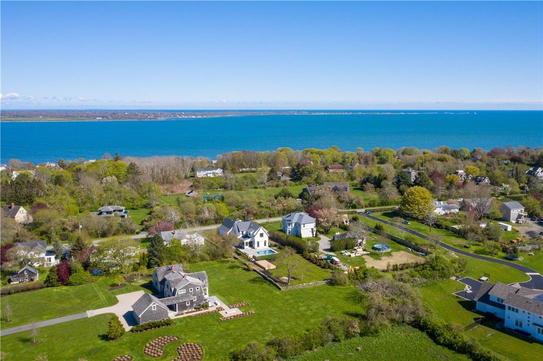 Aerial view of waterfront homes on a green grassy hill, overlooking a blue bay. Bright, sunny day.