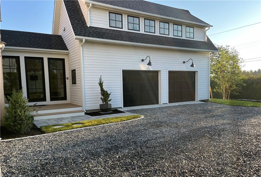 White house with black garage doors, gravel driveway.
