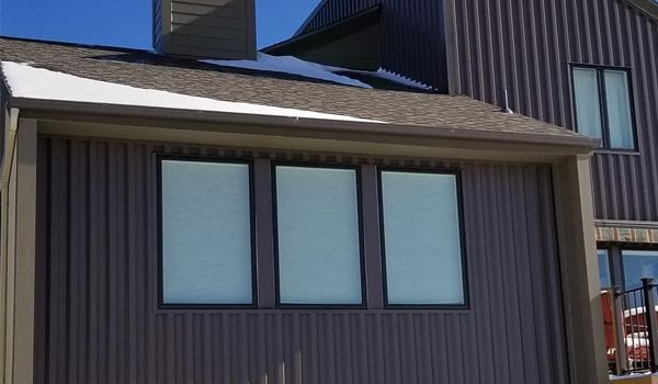 Brown building with vertical siding, three tall windows, and a dark roof.