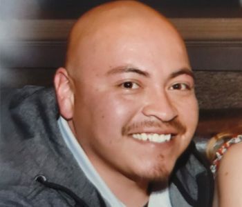 Bald man with a mustache and goatee smiles broadly, wearing a gray jacket.