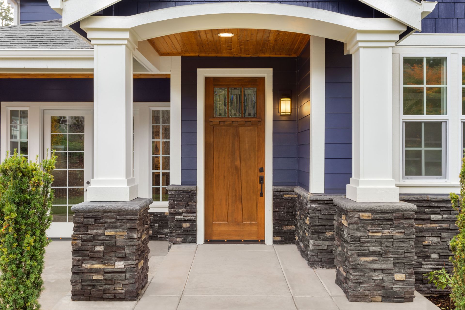 Exterior of a house with a wooden door, blue siding, white pillars, and stone accents.