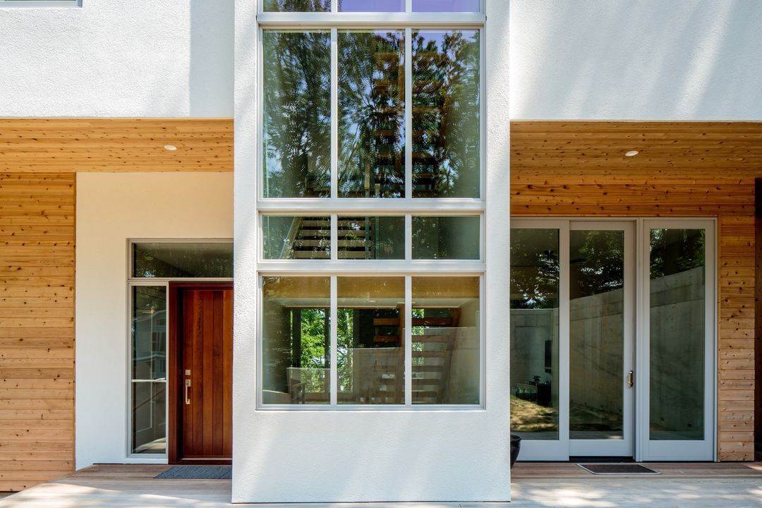 Modern house exterior with large windows, wooden accents, and an open front door.