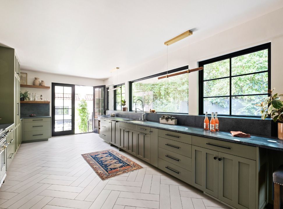 Green kitchen with black-framed windows and doors, blue countertop, herringbone floor, and a rug.