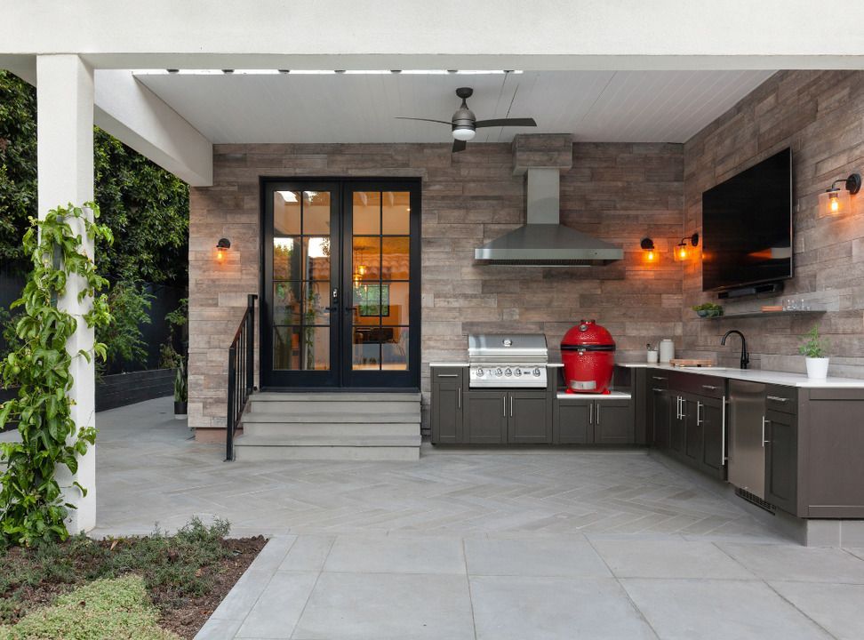 Outdoor kitchen with grill, cabinetry, and a TV on a patio with a covered pergola.