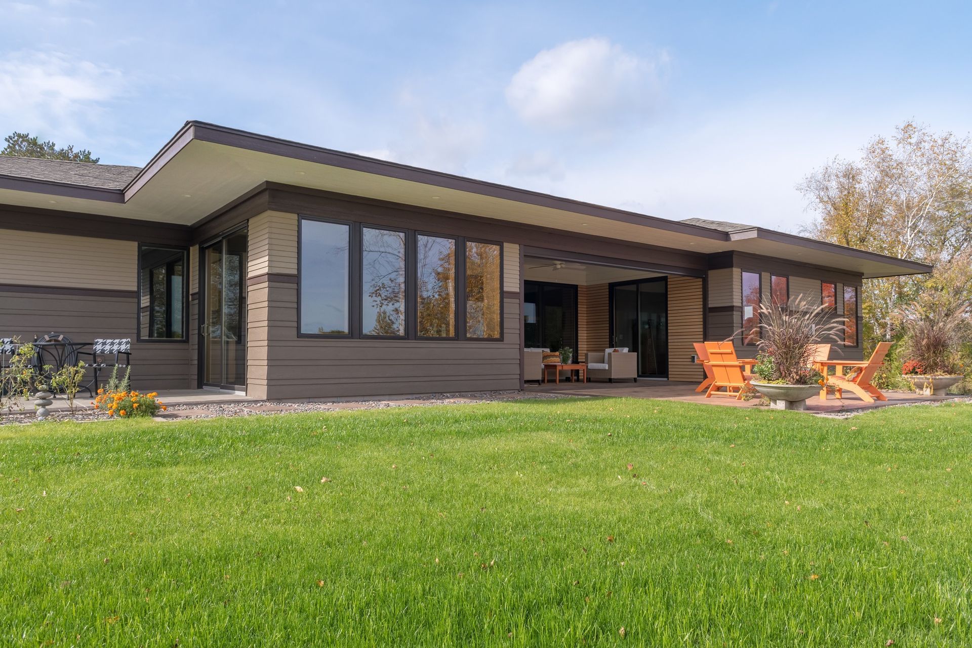 Modern home with large windows, covered patio, orange chairs, and green lawn.