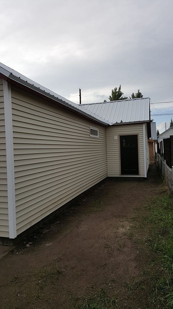Light yellow building with patterned siding, dark door, and metal roof.