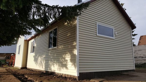Tan house with white-framed windows and vinyl siding. A tree branch hangs in the foreground.