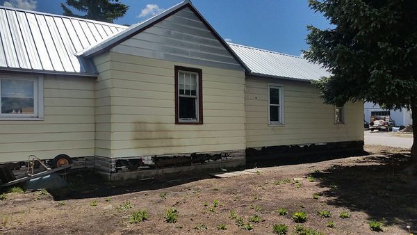 Yellow house with missing siding and visible foundation under a blue sky.