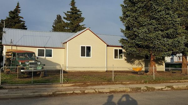 Beige house with a silver roof, a green truck, and a small fence.