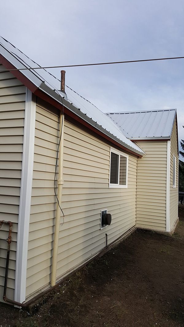 Beige sided house with white trim, metal roof, and window under overcast sky.
