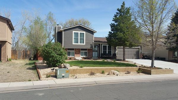 Suburban house with gray siding, two-car garage, and small front yard with retaining wall.