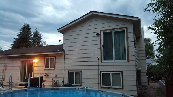 Two-story beige house with a pool in the foreground under a cloudy sky.