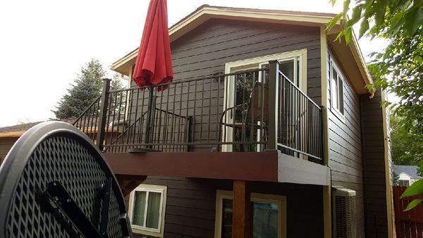 Brown two-story house with a deck. Red umbrella open on the deck, metal railing, dark siding, and windows.