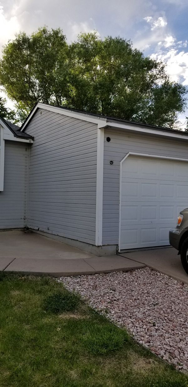 Exterior view of a light gray house with a white garage door, gravel path and a green lawn.