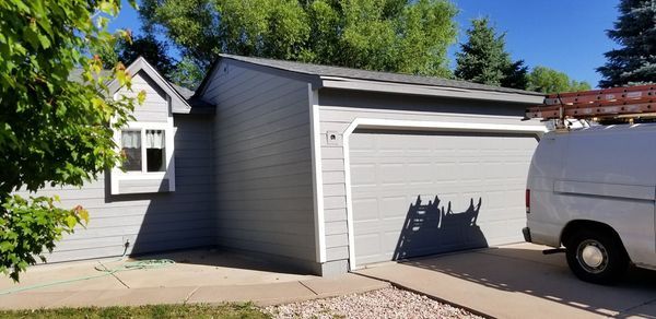 Gray house with a garage and a white van parked in the driveway. Trees and a blue sky in the background.