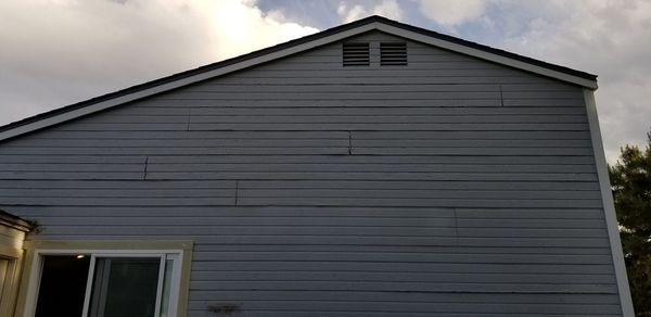 Side of a house with gray siding, a black roof, and a window.