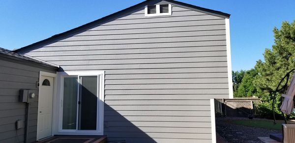 A gray house with white trim, a door, and a sliding glass door against a blue sky.