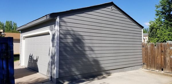 Gray garage with a dark roof and white trim under a clear blue sky.