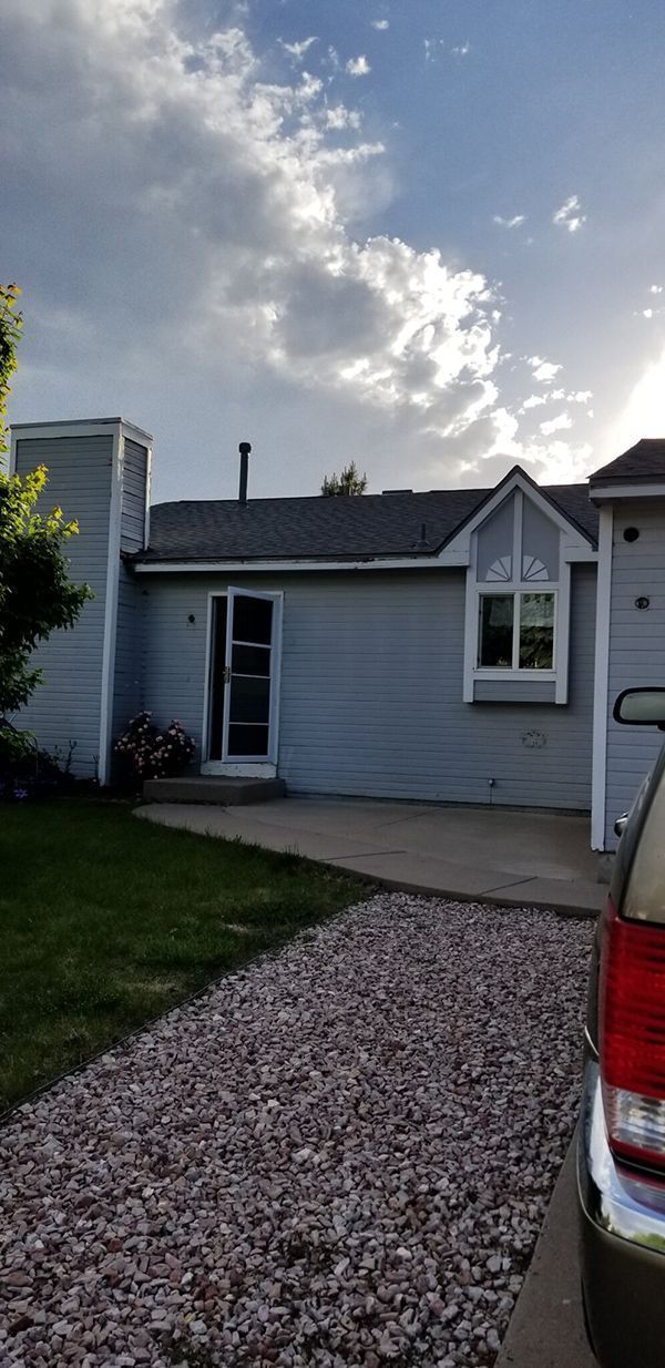 Blue house with a chimney and open door, gravel path, and a car parked on the side. Cloudy sky.