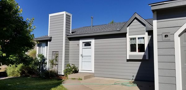 A gray house with a white door, chimney, and trim under a blue sky.