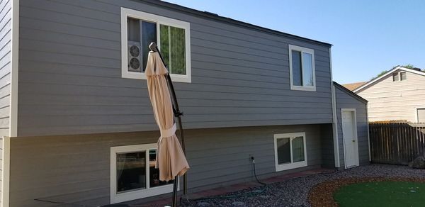 Back of a two-story gray house with multiple windows and a closed patio umbrella in front.