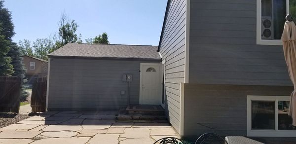 A gray house with a shed and a paved patio on a sunny day.