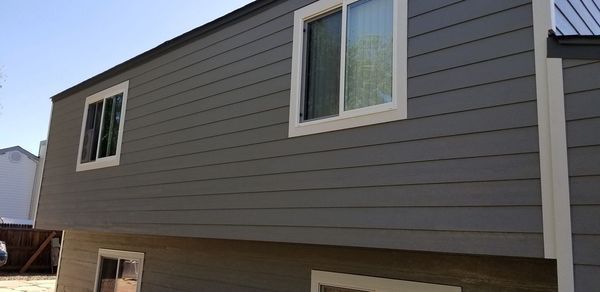 Exterior of a house with gray siding and white-framed windows against a blue sky.