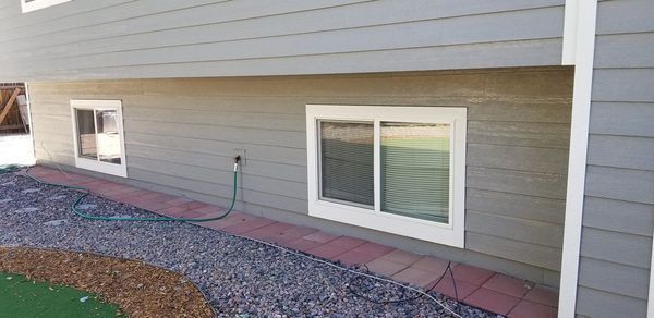 Exterior view of a house with two white-framed windows, gray siding, and a red brick border.