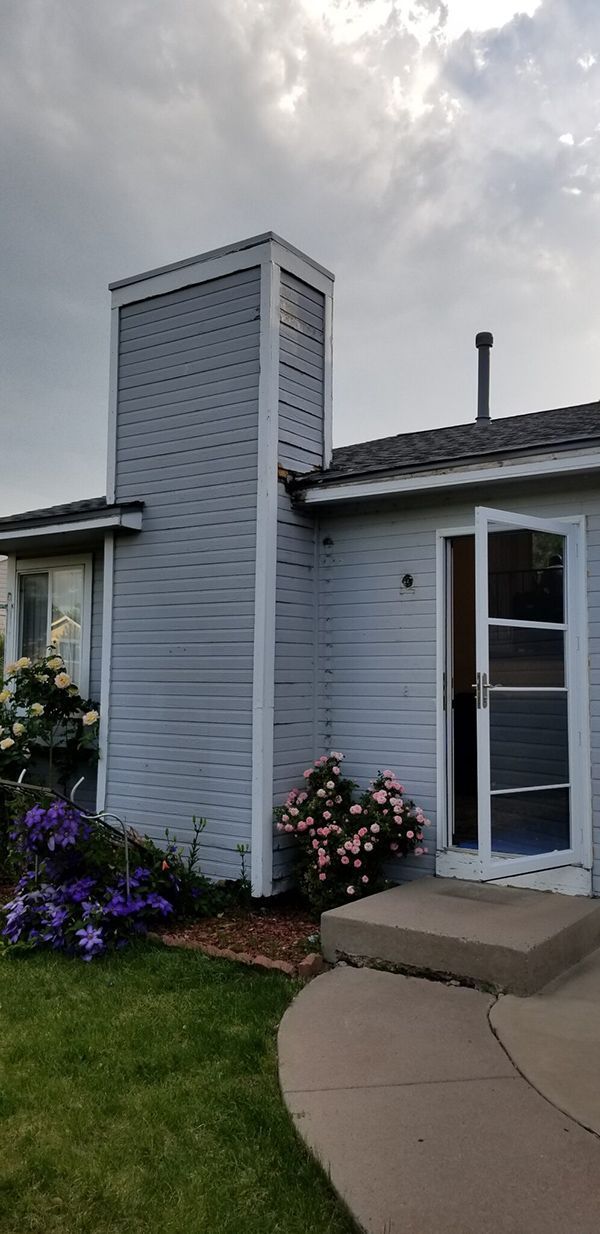 A house with a chimney, open door, and flowers. Cloudy sky.