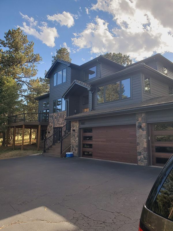 Dark gray house with wood garage doors, stone accents, and deck, set against a blue sky with clouds.