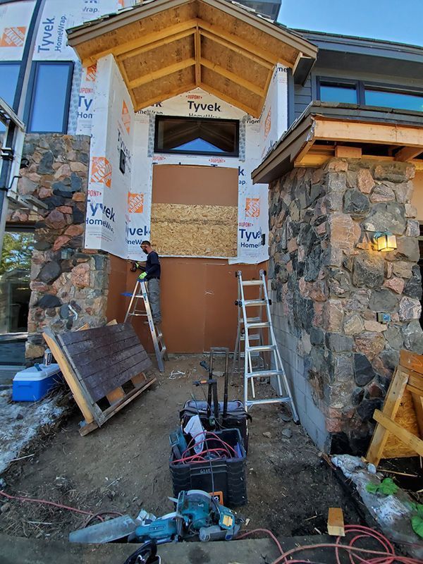 Construction worker on a ladder, installing paneling on a building's entryway, surrounded by tools and materials.