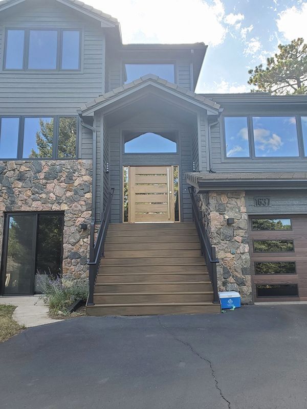 Gray house with stone accents, wooden steps leading to a light wood front door.